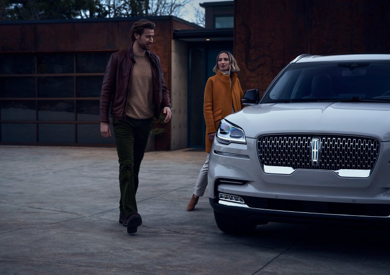 A man and a woman approaching a 2024 Lincoln Aviator® SUV, which illuminates certain lights when they are close | Vista Lincoln Woodland Hills in Woodland Hills CA