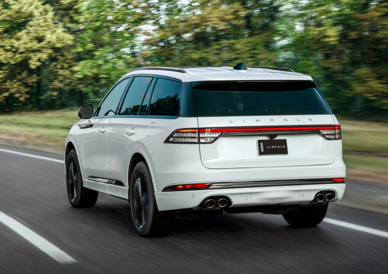 A white 2025 Lincoln Aviator® SUV is being driven away down a road lined with colorful trees. | Vista Lincoln Woodland Hills in Woodland Hills CA