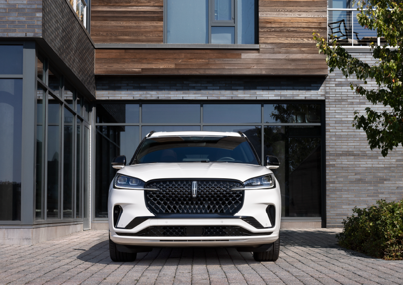 A white 2025 Lincoln Aviator® SUV is shown parked outside a modern building with gray brick and wood accents. | Vista Lincoln Woodland Hills in Woodland Hills CA