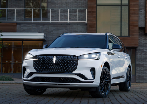 A white 2025 Lincoln Aviator® SUV is shown parked outside a modern building with gray brick and wood accents. | Vista Lincoln Woodland Hills in Woodland Hills CA