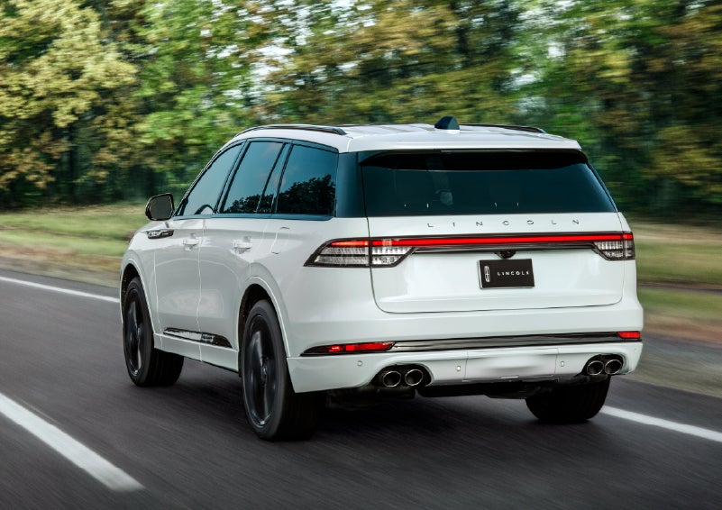 A white 2026 Lincoln Aviator® SUV is being driven away down a road lined with colorful trees. | Vista Lincoln Woodland Hills in Woodland Hills CA